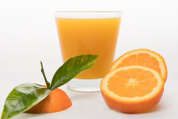 orange juice in glass with pieces of oranges and green leafs on black background. Summer and freshness concept