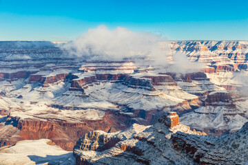 Grand Canyon in the morning, covered in snow. Blue sky; clouds on rim of canyon.
