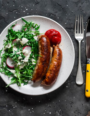 Fried pork sausages and salad with arugula, radish and mustard, yogurt dressing on a dark background, top view