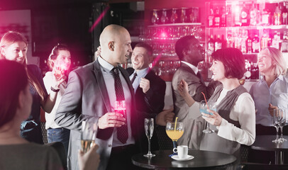 Cheerful glad positive male and female colleagues having fun on corporate party in bar