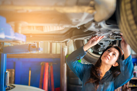 Car mechanic asian woman with spanner tighten car suspension detail of lifted automobile at repair service station. Vintage color tone