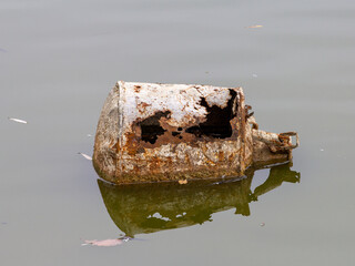 Unidentified metal object in a pond with rusty holes on the body, in a semi-sunken state.