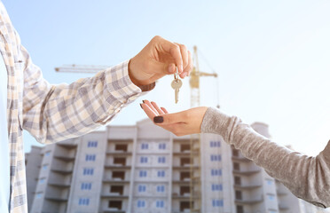 Real estate agent giving a key from new house to woman near unfinished building