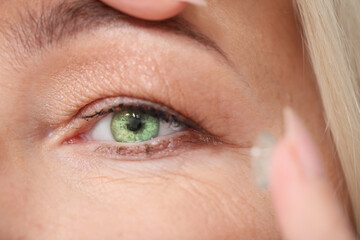 Fototapeta premium Mature woman putting in contact lenses, closeup