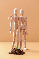 Wooden mannequins with plant in ground on color background