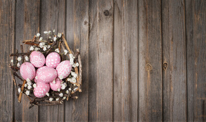 Painted pink easter eggs in the nest build of sticks on vintage old wooden background. Easter card.