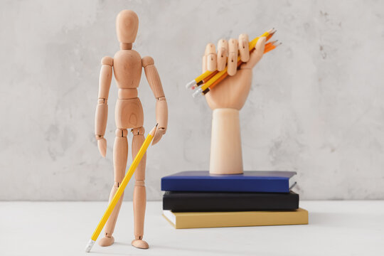 Wooden mannequin with books and pencils on light background