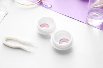 Container with contact lenses and tweezers on light background