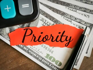 Obraz premium Finance and business concept. Phrase Priority written on red torn paper with calculator,pen and fake money.