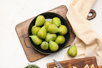 Frying pan with fresh green figs on light background