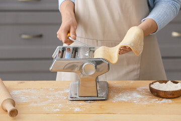 Woman making pasta with machine at table in kitchen