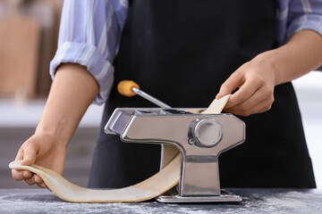 Woman making pasta with machine at table in kitchen