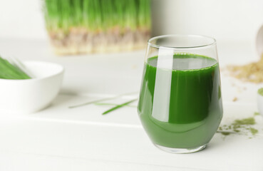 Glass with fresh wheatgrass juice and powder on light background