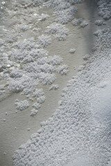 white snowflakes sitting on ice of frozen pond creek on a cold winters day with freezing temperatures and winter climate taken close up vertical format