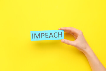 Hand holding paper with text IMPEACH on color background