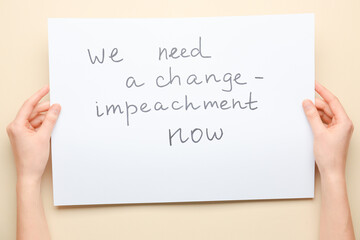 Hands holding paper with text WE NEED A CHANGE - IMPEACHMENT NOW on color background