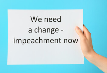 Hand holding paper with text WE NEED A CHANGE - IMPEACHMENT NOW on color background