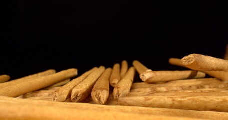 Bakery concept. Scattering of breadsticks. Crunchy sticks on black table. Snacks production conveyor, baked ready. Close up. High quality photo.