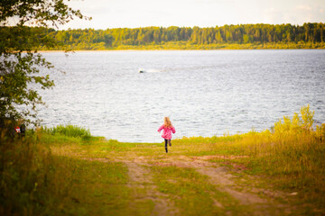 a girl in a pink jacket runs along the road to the river, selective focus