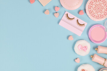 Fototapeta na wymiar Cute pink makeup beauty products like brushes, powder or lipstick on side of pastel blue background with empty copy space