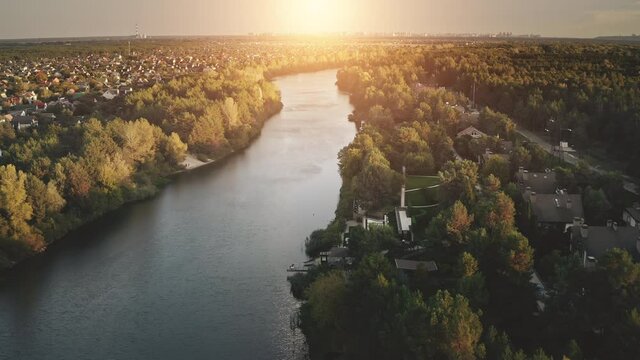 Sunrise over cottages at river shore aerial. Autumn nobody nature landscape. Cityscape buildings at green leaf forest. Urban houses at Dnieper stream, Kiev city, Ukraine, Europe. Cinematic sun rise