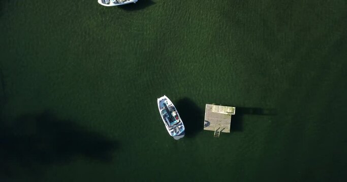 Small wake surfing boat slowly comes into dock on bright sunny day - aerial birds eye view