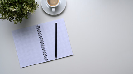 Top view of empty notebook, pencil, coffee cup, plant and copy space on white table.