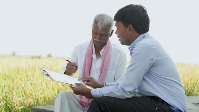 Banker Or Corporate Officer Getting Sign From Farmer While Sitting Near The Farmland - Concept Of Contract Farming, Business Deal And Farm Loan Approval