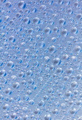 Water drops on blue glass as an abstract background.