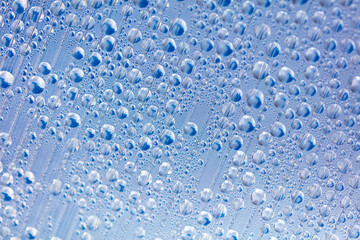Water drops on blue glass as an abstract background.