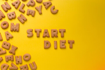 Word Start Diet in the middle of the picture made of tasty crunchy cookies in form of big English alphabet letters, textured bright yellow background, health, dieting and medical concept. Copy space