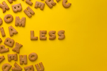 Word Less in the middle of the picture made of tasty crunchy cookies in form of big English alphabet letters, textured bright yellow background, health, dieting and medical concept. Copy space
