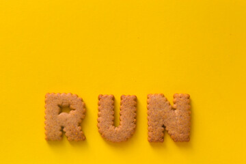 Word Run in the middle of the picture made of tasty crunchy cookies in form of English alphabet letters, textured bright yellow background, health, dieting and medical concept. Copy space, big letters