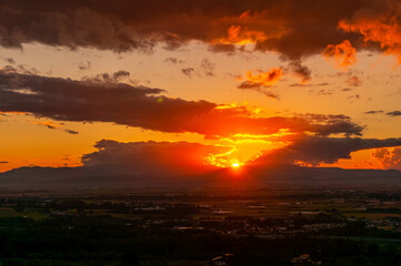 高台から見下ろす真っ赤に焼けた夕日と山なみと街並み