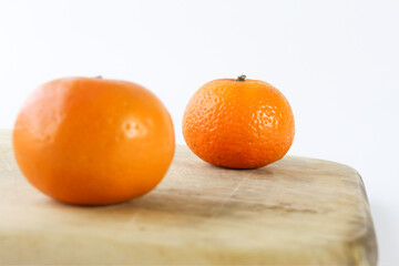 Selective focus of an orange at the back with blurred orange in front of it on the wooden cutting board isolated on white background