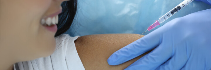 Doctor in rubber gloves injects medicine into shoulder of young woman. Vaccination against coronavirus infection concept.