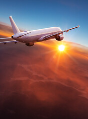 Naklejka na ściany i meble Commercial airplane jetliner flying above dramatic clouds in beautiful light. Travel concept.