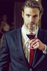 Young man in formal outfit with red tie hold wine glass near woman.