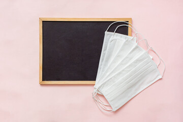 Black letter board for text notes with surgical medical face masks on pink background. Top view, flat lay