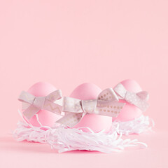 Cute easter eggs with grey ribbon in white nest on pastel pink background, square.