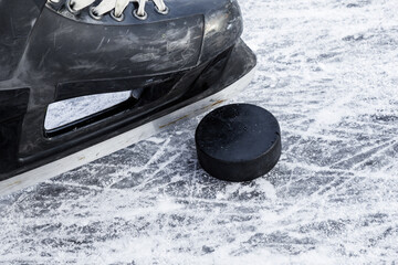 Old black hockey male skate and rubber puck on ice background. Closeup.