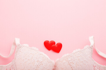 Woman bra and two bright red hearts on light pink table background. Pastel color. Closeup. Empty...