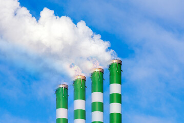 Four Industrial smoke pipes from chimney on blue cloudy sky.