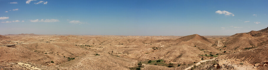 Fototapeta na wymiar Beautiful idyllic far panoramic view over the deserts in north africa in tunasia showing hills, dunes, nature and a wide horizon with blue sky and few clouds.