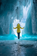 close view of a girl in a yellow jacket stands at the exit of the Baikal lake ice cave in bright light