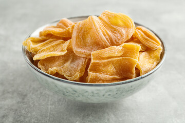 Delicious dried jackfruit slices in bowl on light grey table, closeup