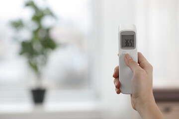 Closeup view of woman with infrared thermometer on blurred background, space for text. Checking...