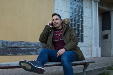 smiling man sitting on the bench using the phone