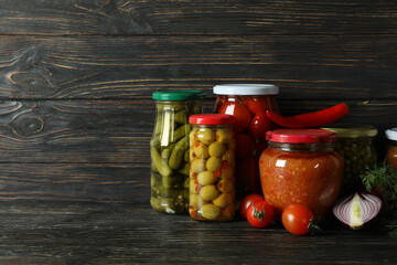 Jars with different canned food on wooden background