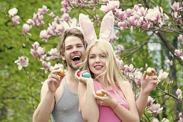 Smiling happy easter couple with bunny ears hold eggs on blossom nature outdoor.